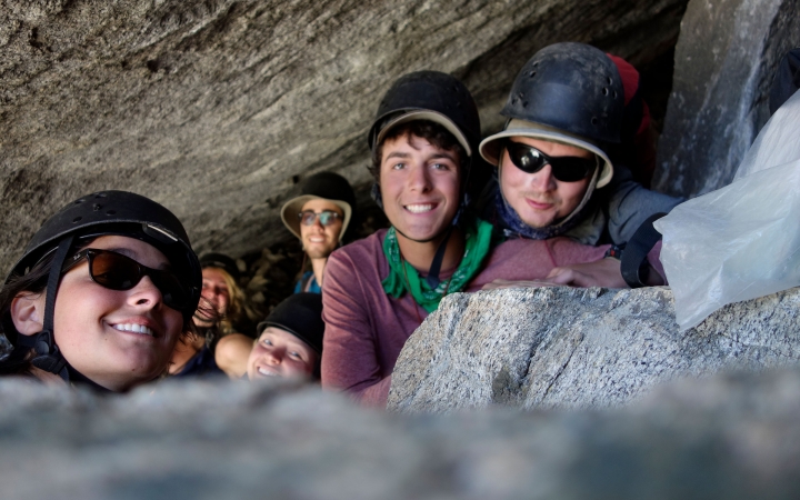 Six people smile at the camera while resting between boulders